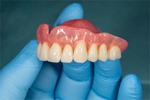 Close-up of gloved hand holding denture for upper arch