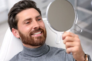 male dental patient holding hand mirror, admiring his teeth