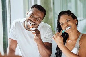 Couple standing in bathroom, brushing their teeth