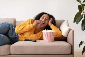 Woman lounging on sofa, eating popcorn