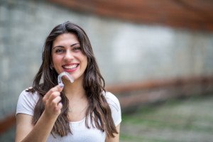 Happy woman in white t-shirt holding a clear aligner