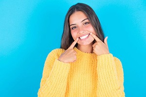 Woman in yellow sweater showing off her teeth after Invisalign treatment